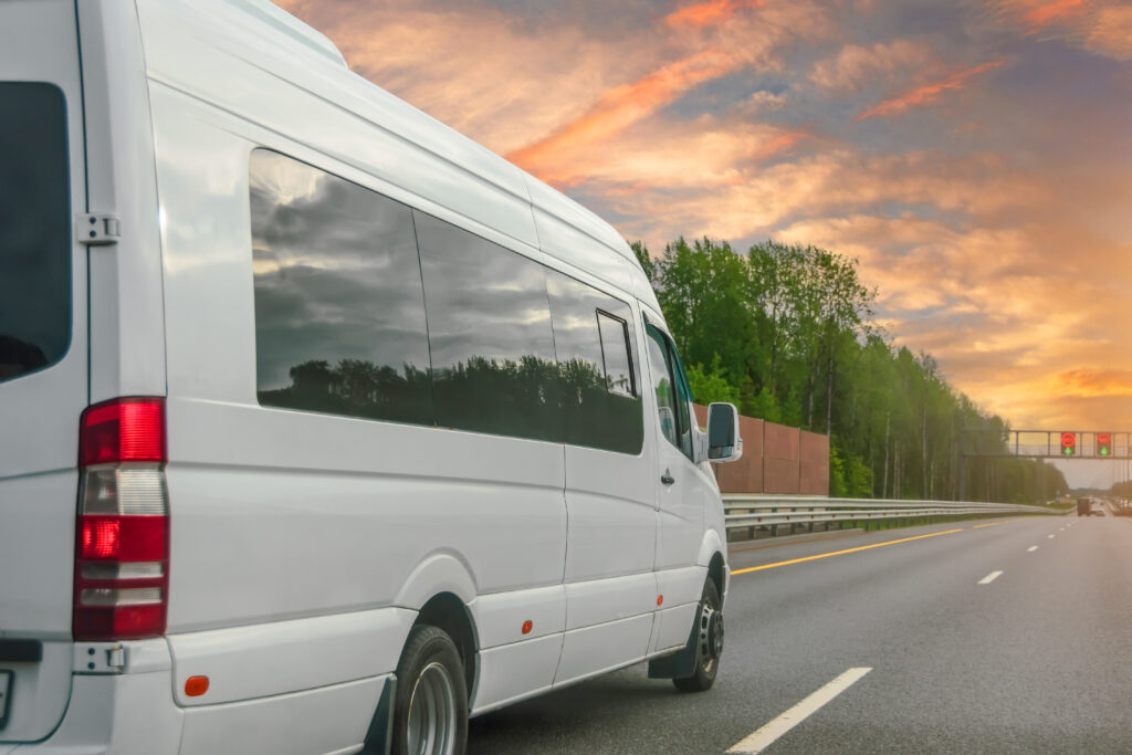 A white used minivan drives on the highway